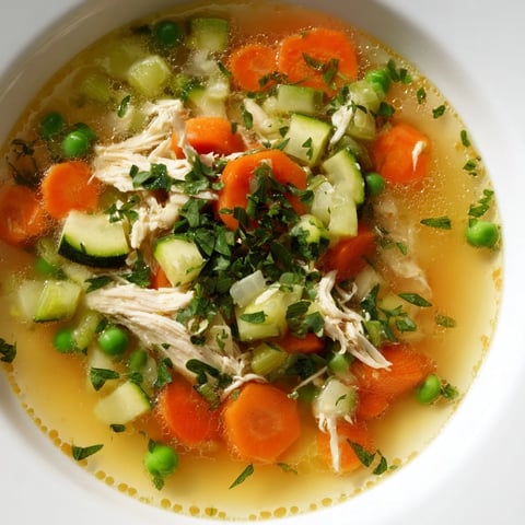 Steaming Spring Garden Chicken Soup features tender shredded chicken, carrots, zucchini, and peas in a clear, herb-infused broth.  