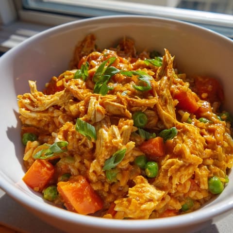 Steaming hot Butter Chicken Fried Rice is plated with vibrant green peas and carrots, garnished with fresh scallions for a colorful, comforting fusion meal.