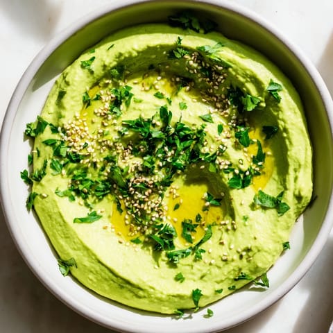 Bright green edamame hummus in a ceramic dish, surrounded by crisp pita chips and colorful raw vegetables for dipping.  