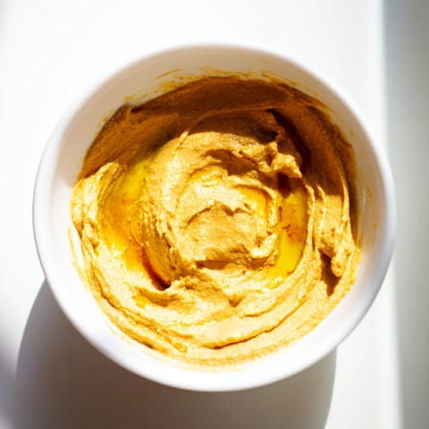 A golden-hued Chickpea Curry Paste served with pita bread and colorful vegetable sticks on a rustic wooden table.  