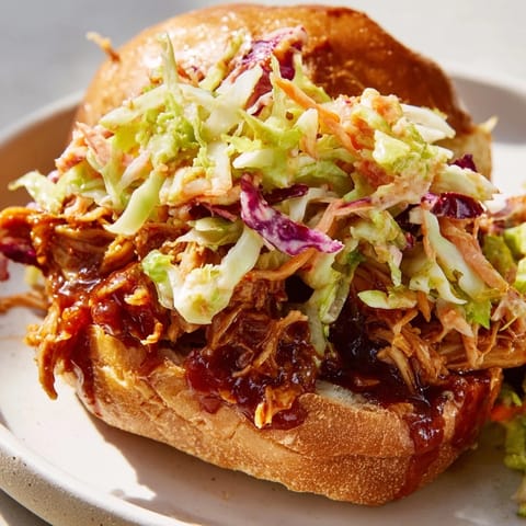 A close-up of a juicy pulled barbecue chicken sandwich with a vibrant red slaw on a soft brioche bun, ready to be enjoyed.