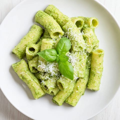 A white bowl filled with warm Creamy Avocado Pesto Mac, featuring a luscious avocado pesto sauce and lemon zest.