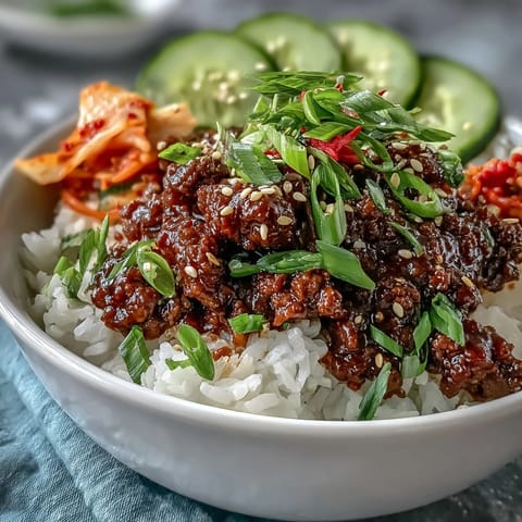 A close-up of Korean Beef Bowl with saucy beef, pickled carrots, cucumber slices, and sesame seeds over steamed rice.