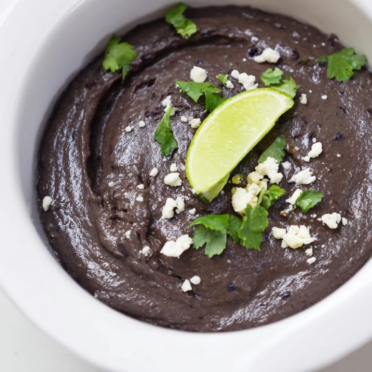 Close-up of smooth Spicy Black Bean Dip topped with sliced jalapeños, served alongside crunchy vegetable sticks.  