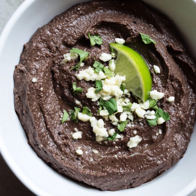 Vibrant bowl of vegan Spicy Black Bean Dip with a sprinkle of cotija cheese, paired with colorful taco night accompaniments.