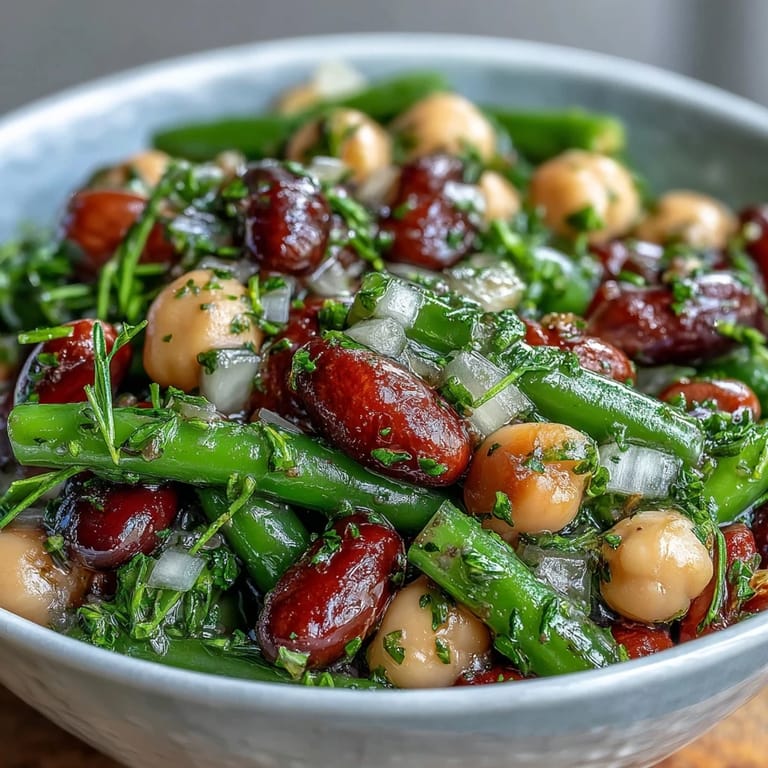 Colorful Three-Bean Salad served chilled in a white bowl, topped with diced red onion and fresh parsley.  
