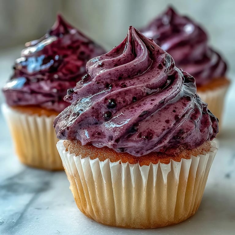 Swirled Black Currant Frosting decorates a cupcake, its deep purple hue vibrant against a clean white liner.